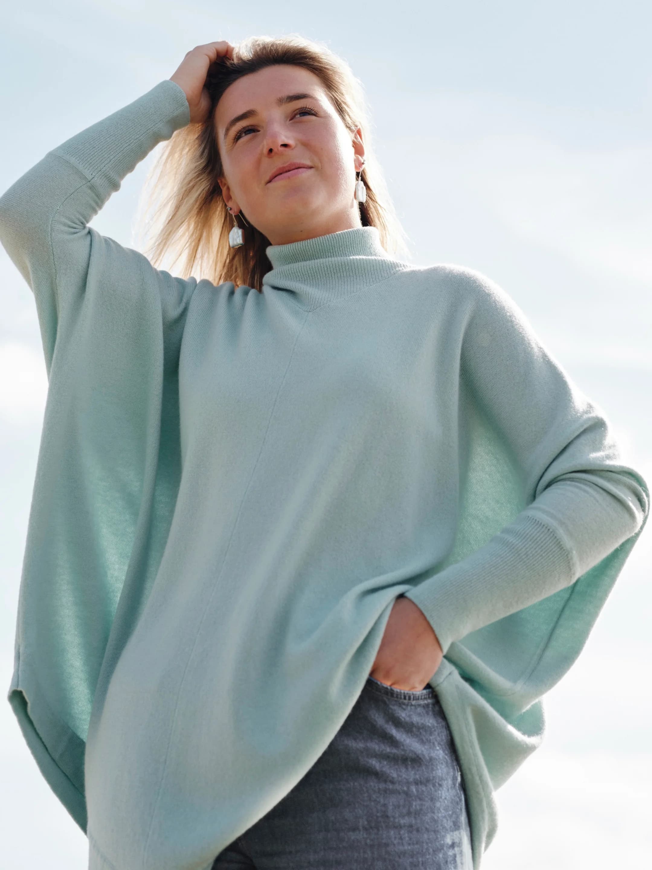 Model outdoors wearing a mint green batwing turtleneck cashmere poncho with ribbing